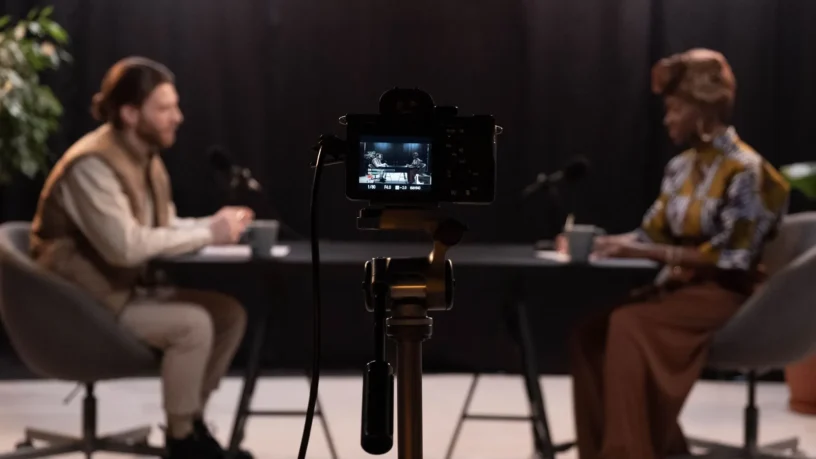 Deux animateurs enregistrent un balado en studio, une caméra au premier plan entre les micros