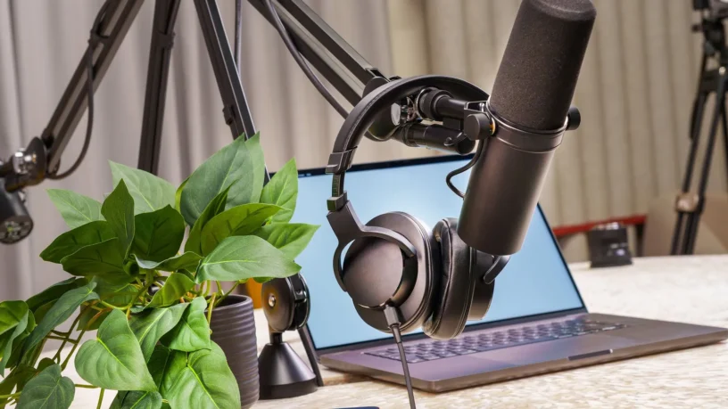 Micro de balado sur bras articulé, casque d'écoute et ordinateur portable sur une table, avec une plante verte