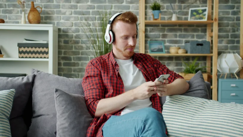 Un homme détendu, casque d'écoute sur la tête, consulte son téléphone dans son salon
