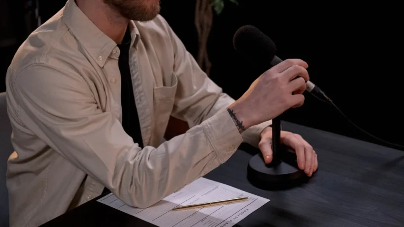 Un animateur lit ses notes au micro, crayon à la main, dans un studio sombre